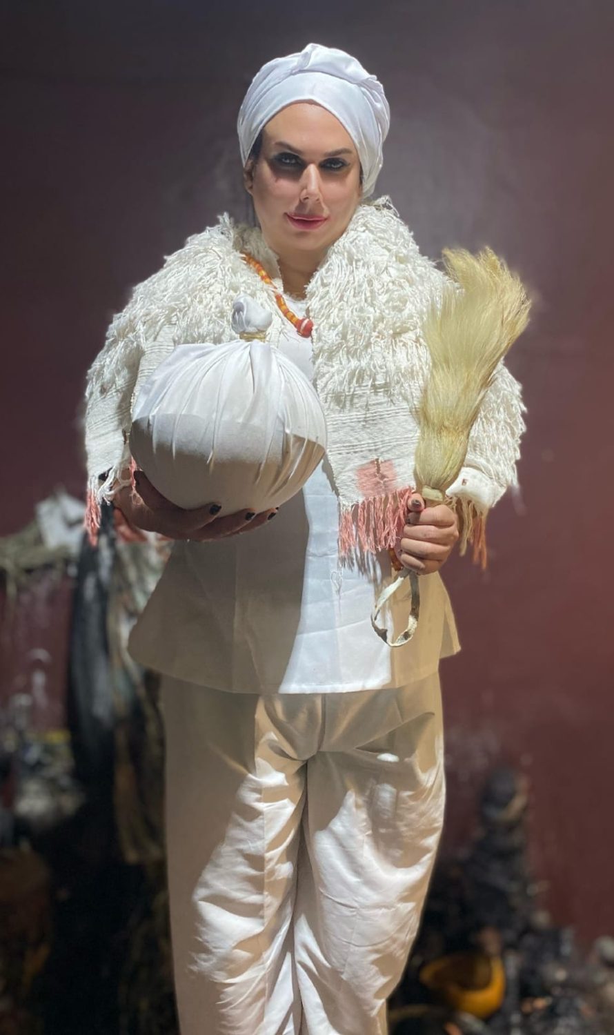 Dirigente do Templo da Serpente Negra em traje ritual branco com turbante e objetos cerimoniais